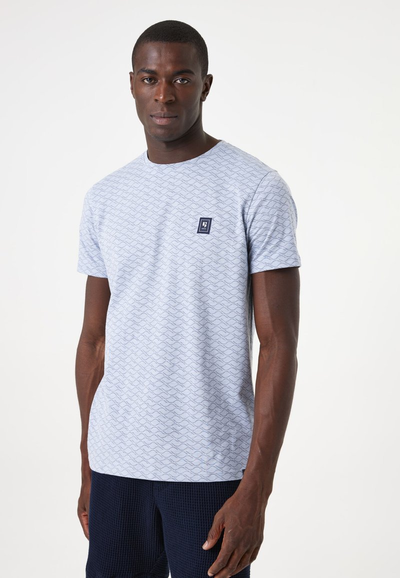 Camiseta azul clara con patrón de olas, cuello redondo, mangas cortas y un pequeño parche de logo en marino en el lado izquierdo del pecho. Tejido de algodón suave.