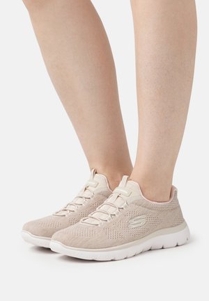 Ljusbeige mesh-sneakers med en texturerad ovandel, elastiska snören, en vadderad krage och en vit gummisula med vågmönster.