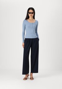 Light blue ribbed long-sleeve top with button accents, paired with navy wide-leg trousers and brown heeled sandals.