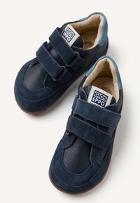 Sneaker blu navy con parte superiore in suede e pelle testurizzata, dotate di due cinturini in velcro, punta arrotondata e suola in gomma marrone.