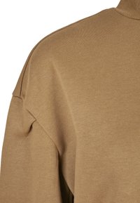 Hanorac maro cu o țesătură texturată, având un guler înalt, umeri lăsați și un design moale, casual.