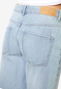 Shorts in denim azzurro chiaro con vita alta, caratterizzati da due tasche posteriori e un'etichetta in pelle beige. I dettagli di cucitura semplici e classici sono ben visibili.