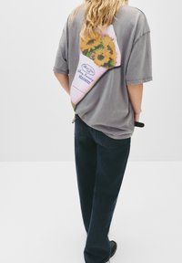 Šedé přešité tričko z bavlny s živou grafikou květinové kytice na zadní straně, doplněné tmavými denímovými kalhotami.