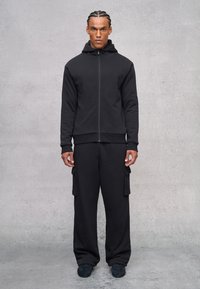Felpa nera con cappuccio e pantaloni cargo coordinati realizzati in tessuto morbido. La felpa presenta una chiusura con zip e una vestibilità comoda; i pantaloni hanno tasche laterali.
