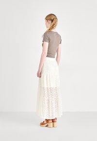 Top corto de manga corta marrón combinado con una falda maxi de encaje crema con volantes. La falda presenta un patrón texturizado y una cinturilla ajustada. Sandalias de plataforma marrones.
