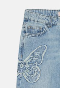 Light blue denim jeans with a faded texture feature a large embroidered butterfly design on the left thigh. Small front pocket included.