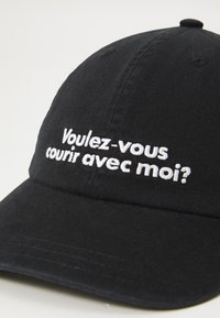 Juodas medvilninis beisbolo kepuraitė su baltu siuvinėtu užrašu "Voulez-vous courir avec moi?" priekyje ir išlenktu snapeliu.