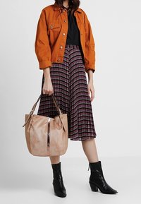 Giacca in denim marrone, top nero, gonna plissettata con motivo viola e nero, borsa beige con accents metallici e stivali neri con tacco.
