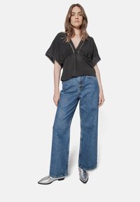 Black short-sleeve top with a V-neck and lace trim, paired with high-waisted wide-leg blue denim jeans and silver pointed-toe shoes.