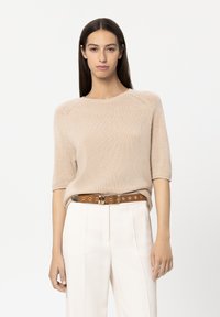 Beige knitted sweater with short sleeves, round neckline, and subtle texture, paired with cream trousers and a brown belt featuring gold accents.