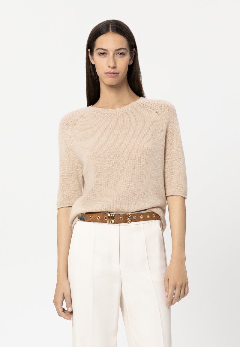 Beige knitted sweater with short sleeves, round neckline, and subtle texture, paired with cream trousers and a brown belt featuring gold accents.