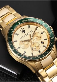 Guld-tone Maserati ur med en grøn tachymeter-lunette, cremefarvet urskive, tre sub-dials, sorte accenter og et guld-link armbånd. Vandafvisende.