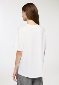 Biała koszulka z krótkim rękawem, okrągłym dekoltem, luźnym krojem i gładką fakturą, zestawiona z szarymi spodniami w kratę.