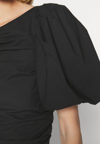 Svart topp med puffärmar som har en draperad design, texturerad tyg och samlade detaljer längs sidan för ökad form och dimension.