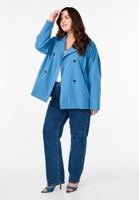 Blå dubbelknäppt kappa med stora svarta knappar, lös passform, i kombination med mörka jeans och blå klackar. Slät tyg, skräddarsydd design.