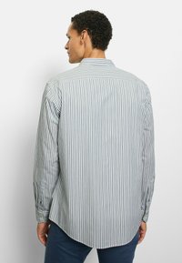 Langärmeliges gestreiftes Hemd in Hellblau und Weiß mit spitzem Kragen, geknöpften Manschetten und abgerundetem Saum. Strukturierter Baumwollstoff.