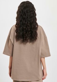 Overdimensjonert beige bomulls t-skjorte med korte ermer; har rund hals og løs passform. Glatt tekstur, minimal detaljering og rett falset.