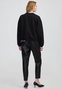 Czarny krótki sweter z szerokimi rękawami, zestawiony z dopasowanymi czarnymi spodniami z sztucznej skóry oraz czarnymi szpilkami z subtelnym akcentem na obcasie.