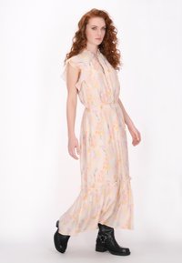 Maxikleid aus leichtem Blumenstoff, mit Rüschensäumen, einem taillierten Gürtel und einem gestuften Rock; kombiniert mit schwarzen Stiefeletten.