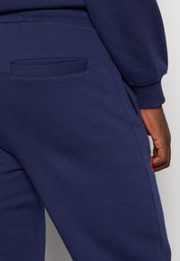 Marinblå sweatpants med bakficka, elastisk midja och ribbade manschetter. Mjukt material med minimala designdetaljer och röd logotypdetalj.