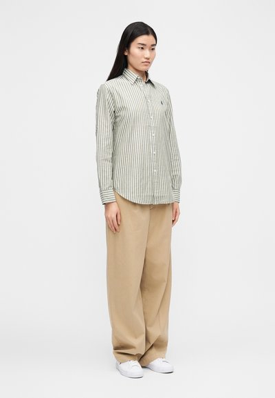 Košeľa na zapínanie so zeleno-bielymi vertikálnymi pruhmi, dlhými rukávmi a priliehavým strihom. Kombinovaná s voľnými béžovými nohavicami a bielymi teniskami.