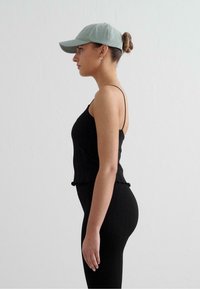 Svart ribbad crop top med tunna axelremmar och volangkant, kombinerad med svarta tajta leggings. Avslutad med en ljusgrön basebollkeps.