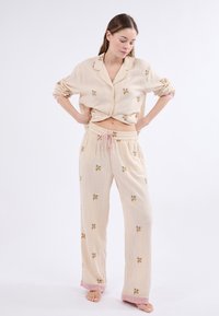 Gestreept pyjamastel in zacht beige, met bloemenborduursel, knoopsluiting bovenkant en broek met koordje in de taille, met roze accenten bij de manchetten.