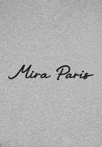 Texte cursif noir "Mira Paris" brodé sur un fond de tissu gris clair.