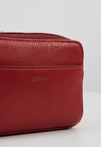 Punainen nahkalaukku, jossa on teksturoitu pinta, hopeinen "DAY ET" -logo ja vetoketjullinen suljenta yläreunassa.