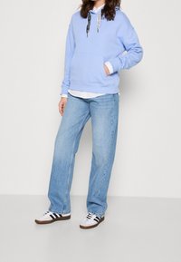 Person som bär en ljusblå hoodie med kontrasterande svarta och vita snoddar, ljusblå jeans, vita sneakers med svarta ränder.