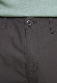 Schwarze Hose mit strukturiertem Finish, mit Knopfverschluss, geraden Taschen und kontrastierenden Nähten.
