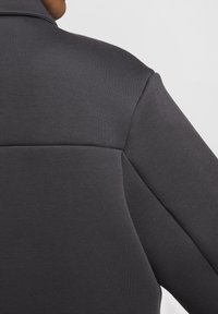 Szara kurtka z tkaniny o gładkiej fakturze, posiadająca usztywniany kołnierz oraz wyraźne przeszycia na plecach, podkreślające dopasowany krój.