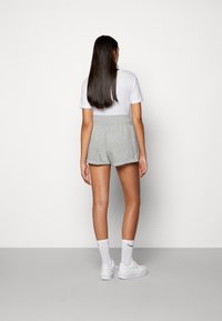 Pantalones cortos de algodón gris con una textura suave, cinturilla elástica y costuras laterales. Llevados con una camiseta blanca y zapatillas deportivas blancas.