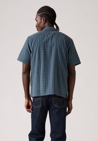 Korte mouwen button-up shirt in donkerblauw met een wit en aqua ruitpatroon. De stof is glad; het shirt heeft een klassieke kraag en een achterpand.