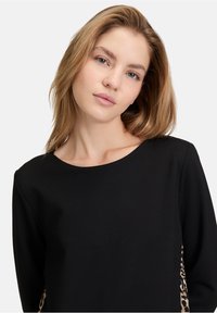 Top nero a maniche lunghe con scollatura rotonda, decorato con dettagli in stampa leopardata sui lati e una texture morbida.
