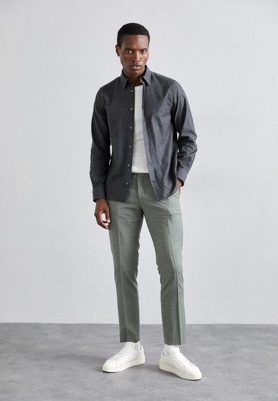 Gray button-up shirt layered over a white crew neck, paired with light green tapered trousers and white sneakers on a gray background.