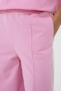 Ružové joggingové nohavice vyrobené z jemnej zmesi bavlny, s elastickým pásom, bočnými vreckami a bielymi bočnými akcentmi.