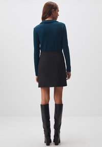 Maglietta a maniche lunghe color teal con colletto, abbinata a una gonna nera e stivali neri fino al ginocchio. Tessuto liscio e design aderente.