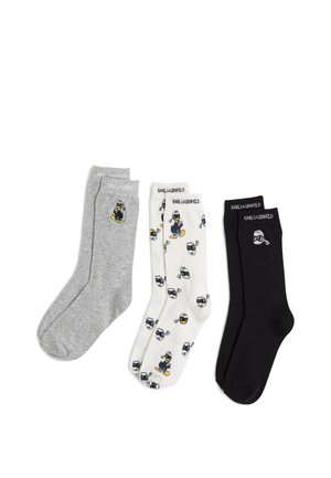 Drei Paar Socken: grau mit Grafik, weiß mit schwarzen Cartoon-Charakterdrucks und einfarbig schwarz, alle mit Karl Lagerfeld-Branding.