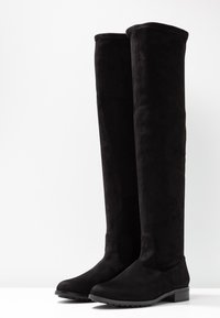 Stivali neri alti fino al ginocchio, realizzati in morbido suede, con punta rotonda e tacco basso a blocco, caratterizzati da una superficie testurizzata e decorazioni minimali.