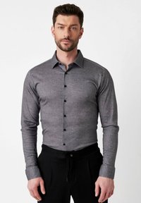 Grau langärmliges Hemd mit Button-Down-Kragen, texturiertem Stoff und schwarzen Knöpfen, kombiniert mit schwarzen Hosen mit Kordelzug.