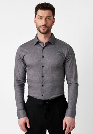 Grijze langslavende shirt met een knoopsluiting kraag, gestructureerde stof en zwarte knopen, gecombineerd met zwarte broek met een trekkoord.
