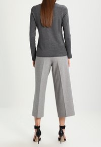 Grijs langmouwsweater gecombineerd met grijze wijde broek met een textuurafwerking en contrasterende zijkanten. Zwarte enkelbandjeshakken.