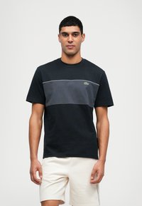 Zwart en donkergrijs katoenen T-shirt met ronde hals, korte mouwen en het Lacoste-logo op de borst. Heeft een horizontaal kleurblokontwerp.