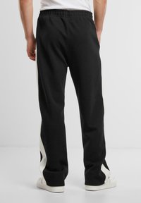 Sorte sweatpants med hvide sidelister, elastisk talje og afslappet pasform. Lavet af blødt stof med en glat overflade.