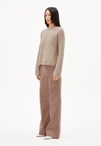 Beige strukturierter Strickpullover mit einem geometrischen Muster, kombiniert mit braunen Cordhosen mit hoher Taille und weitem Bein sowie weißen spitzen Pumps.