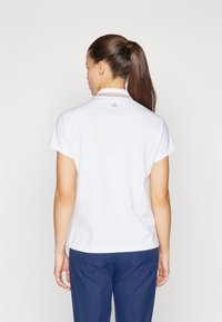 Polo bianco a maniche corte, con colletto e un piccolo logo sul retro. Abbinato a pantaloni blu navy, con una texture di tessuto liscia.