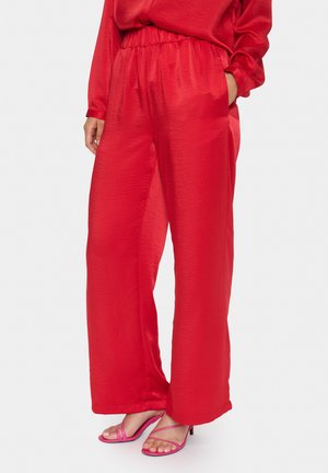 Rode wijde broek van glanzende stof met een elastische tailleband, met zijzakken, gecombineerd met roze sandals met bandjes.