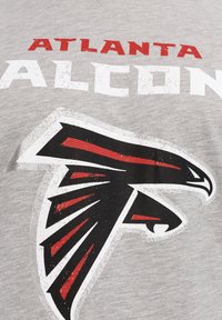 Šedé bavlněné tričko s nápisem "Atlanta Falcons" v červené a bílé barvě, s velkým černým a červeným logem falcona umístěným ve středu pod ním.