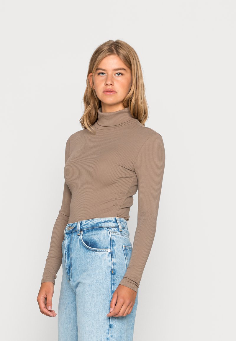 Brauner gerippter Rollkragenpullover mit langen Ärmeln, kombiniert mit hellblauen hochtaillierten Jeans. Glatte Textur und taillierte Passform.
